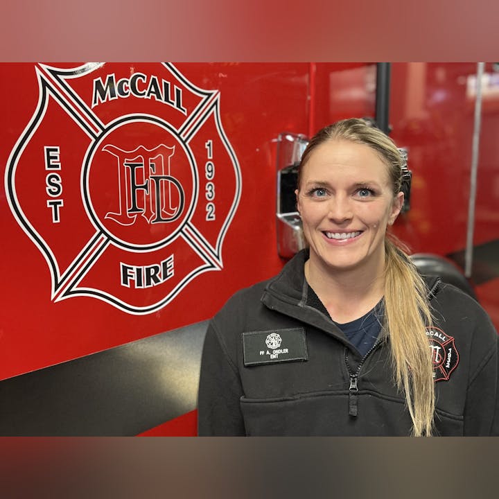 A smiling person in front of a fire truck with a "McCall FIRE" emblem.