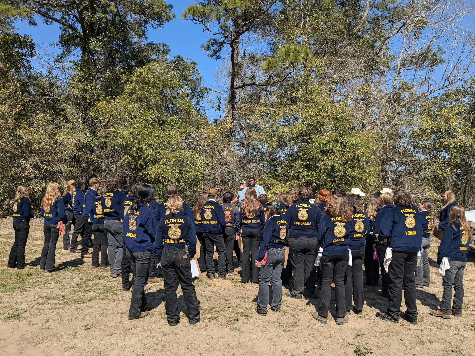 A group of people wearing matching "Florida" jackets stand outside, possibly in a forested area.