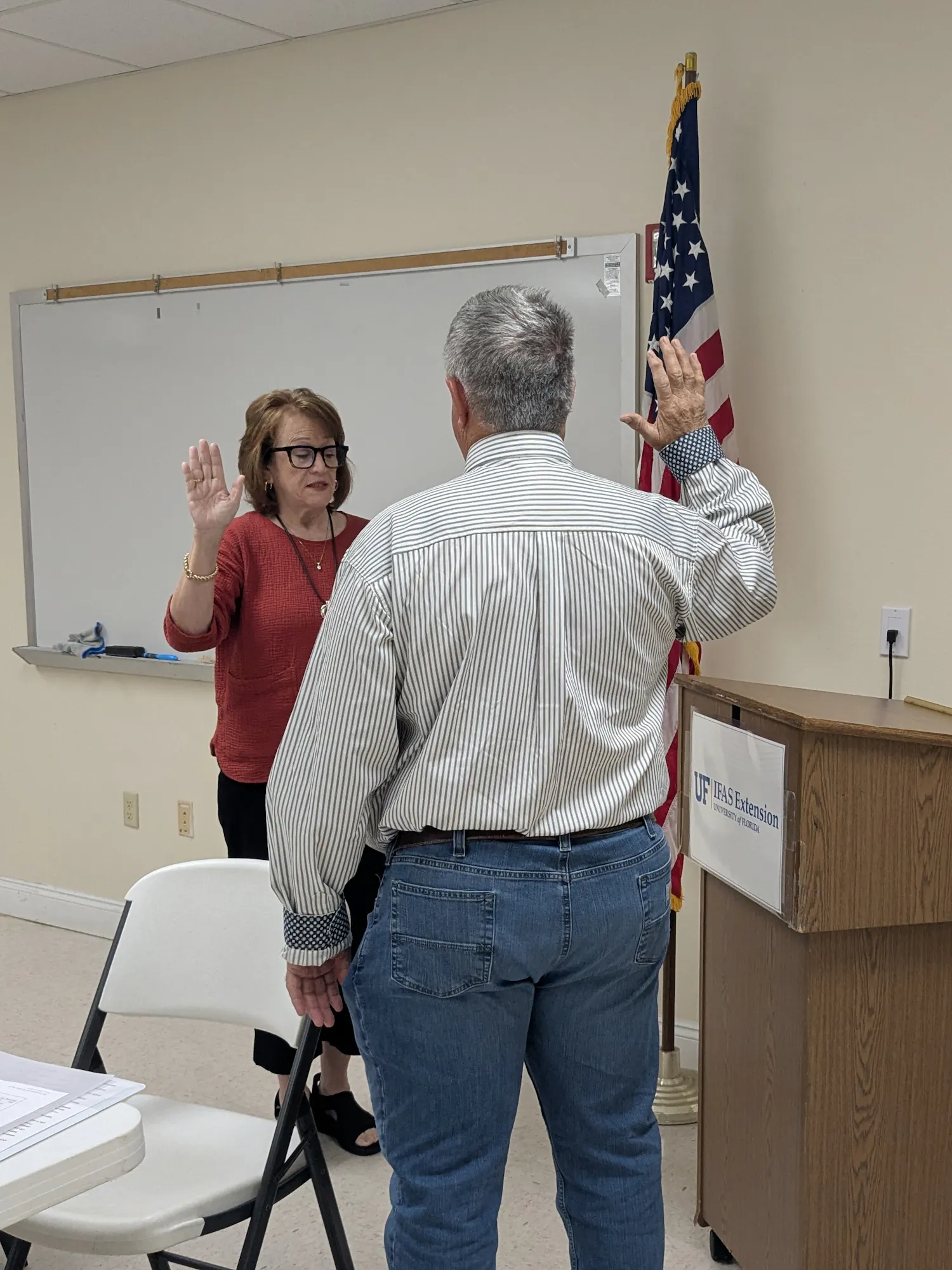A woman administers an oath to a man in a formal setting, with an American flag and a podium in the background.