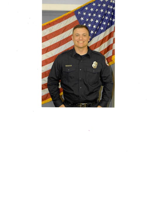 A person in a uniform stands smiling in front of the American flag.