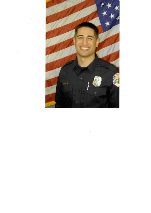 Person in uniform smiling in front of an American flag backdrop.