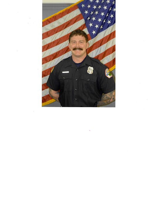 A person in a uniform stands in front of an American flag.