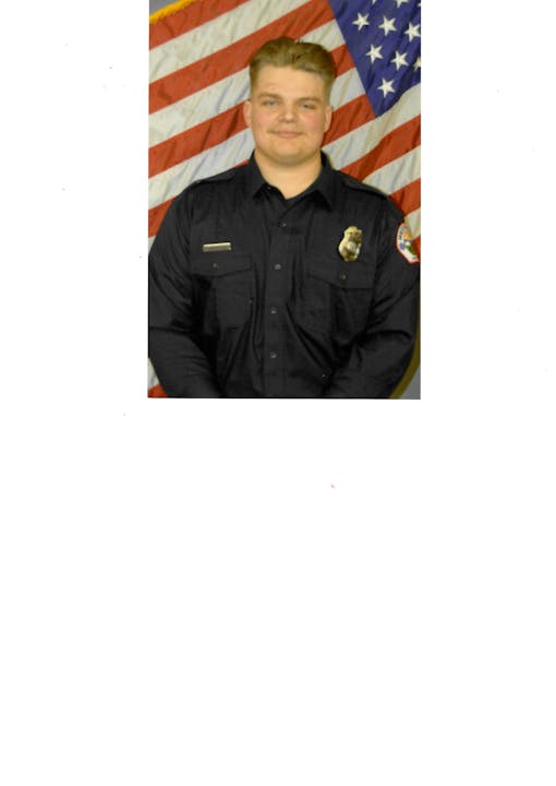 A person in a dark uniform stands in front of the American flag.