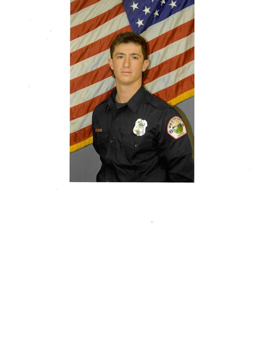 A person in a uniform stands in front of a U.S. flag backdrop.