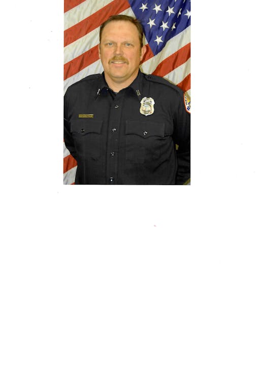 A person in a uniform stands in front of an American flag.