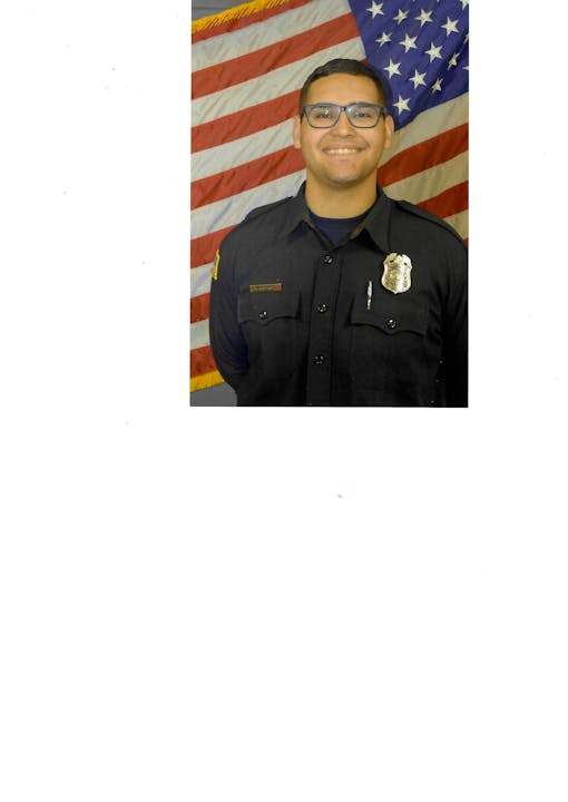 A person in uniform stands smiling in front of an American flag backdrop.
