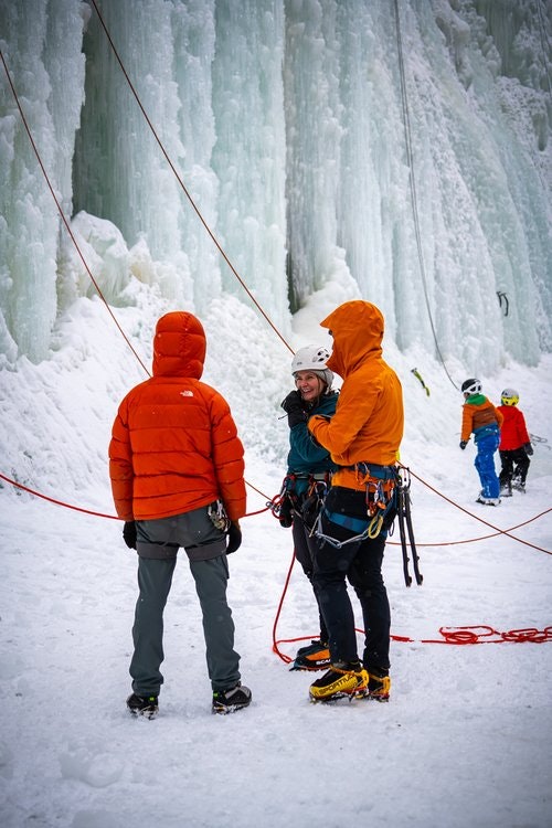 People in winter gear near an ice wall, preparing to climb.