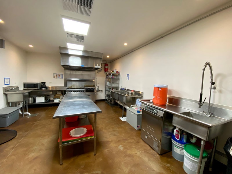 A commercial kitchen with stainless steel appliances, tables, and storage racks.