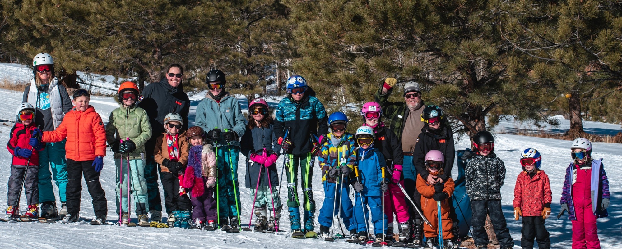 Group of people in winter gear with skis, posing on a snowy slope surrounded by trees.