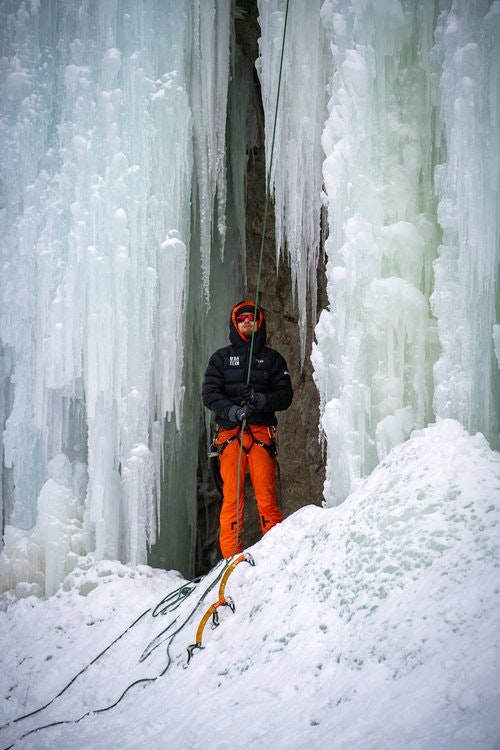 Ice climber standing with gear in front of icicles.