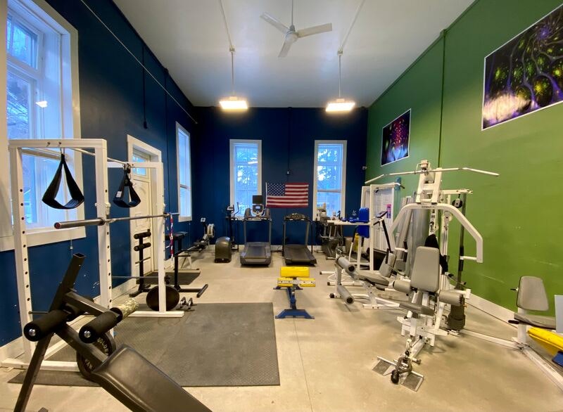 A gym with various exercise equipment, surrounded by blue and green walls, and decorated with photos and a U.S. flag.