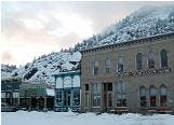 Snow-covered street with historic buildings, a mountain backdrop, and cloudy sky.