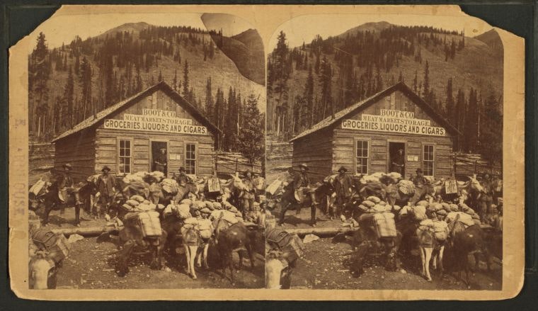 An old photo showing a general store with people and pack animals outside in a mountainous area, likely a mining town.