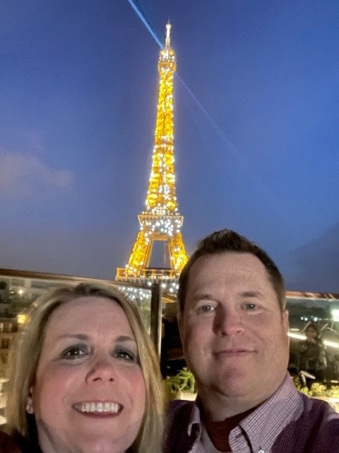 Two people taking a selfie with the illuminated Eiffel Tower at night in the background.