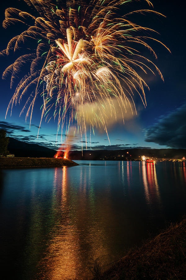 Fireworks display over a calm lake with reflections and a night sky.