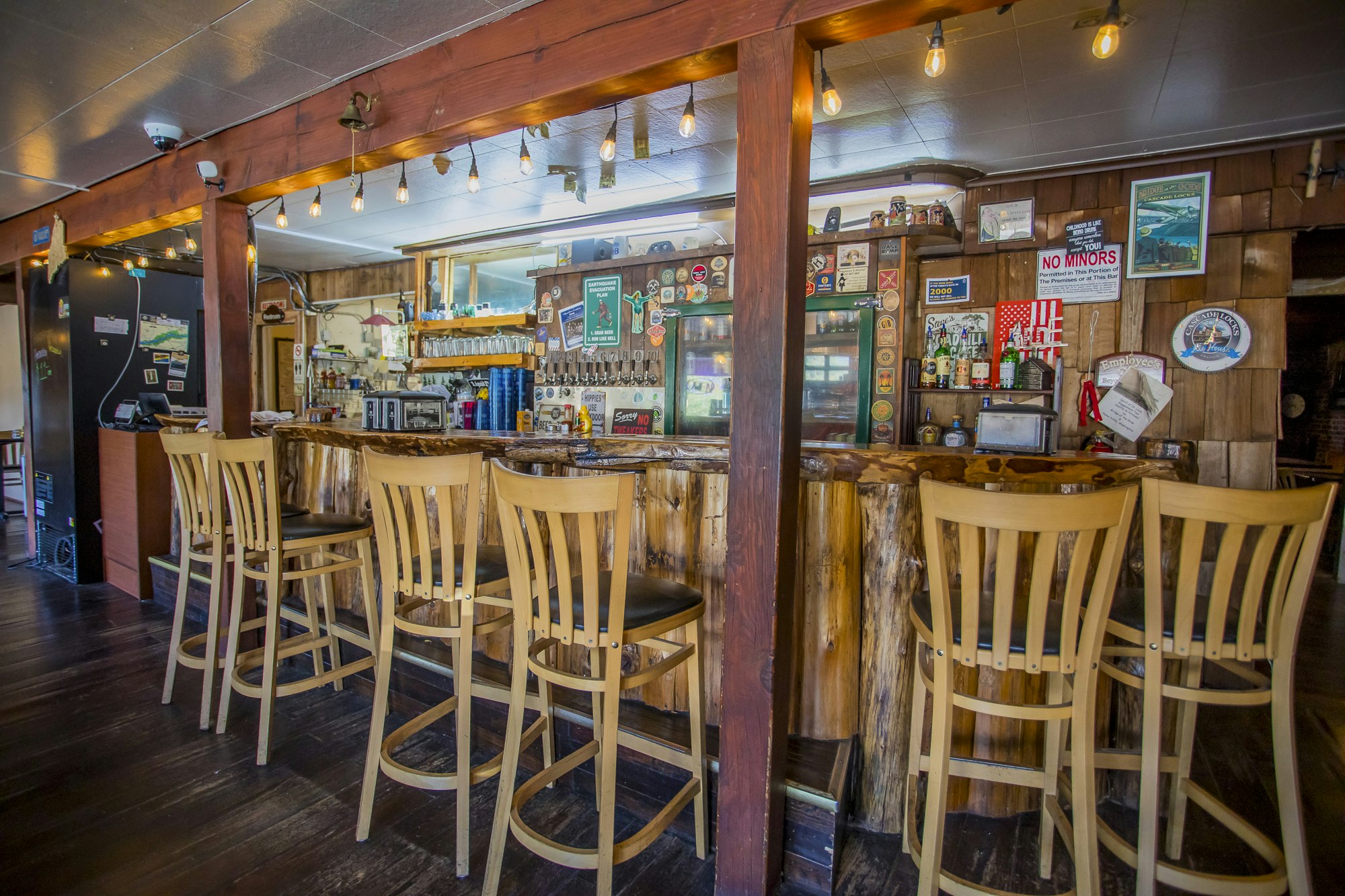 Cozy wooden bar with high chairs, warm lighting, and various signs and decorations on the walls.