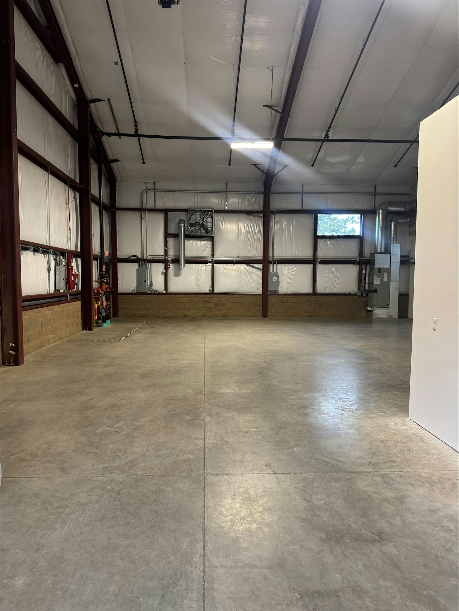 The image shows a spacious, empty industrial-style room with a high ceiling, concrete floor, and exposed metal beams.