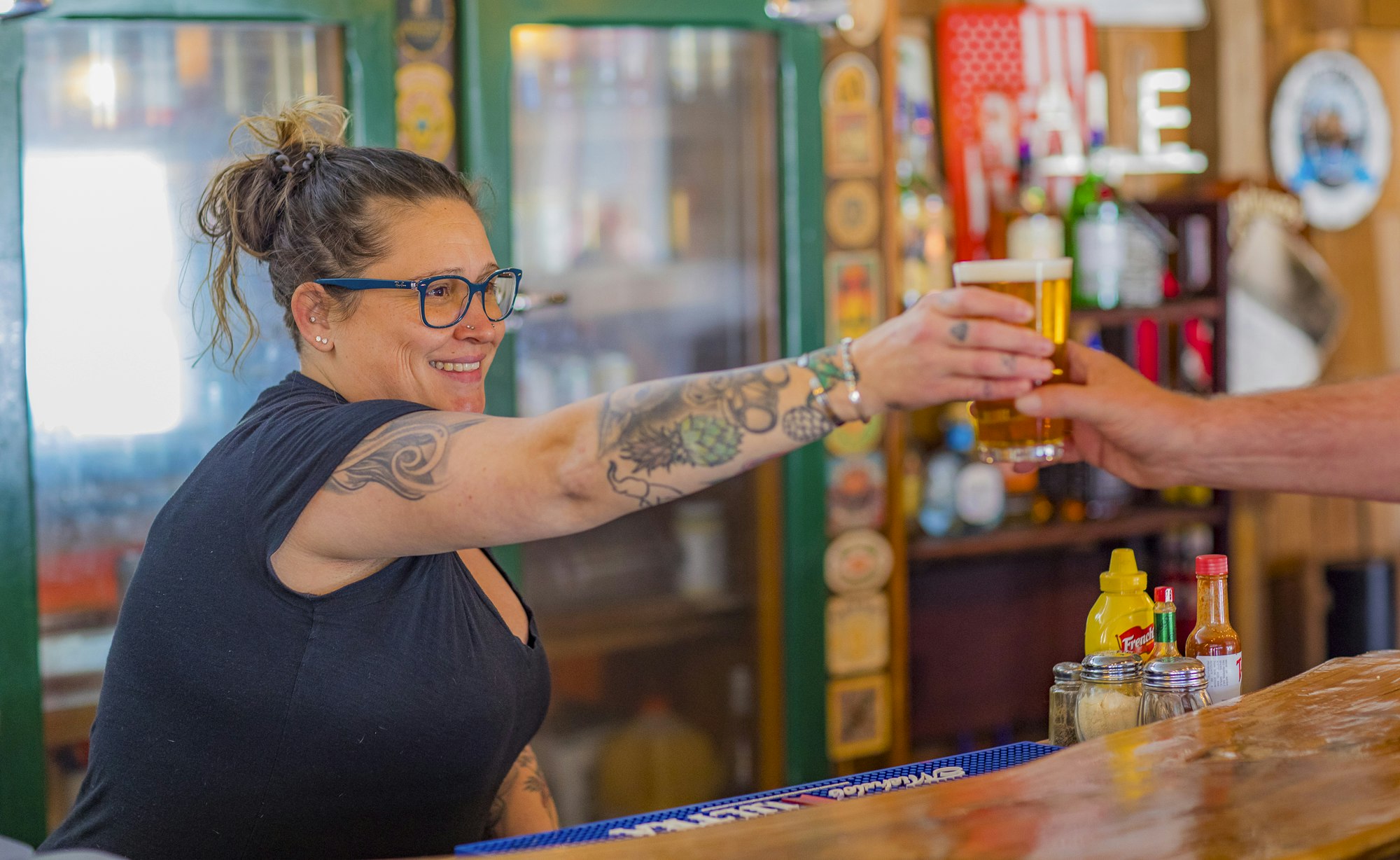 A bartender smiling while handing a glass of beer to a customer at a bar.