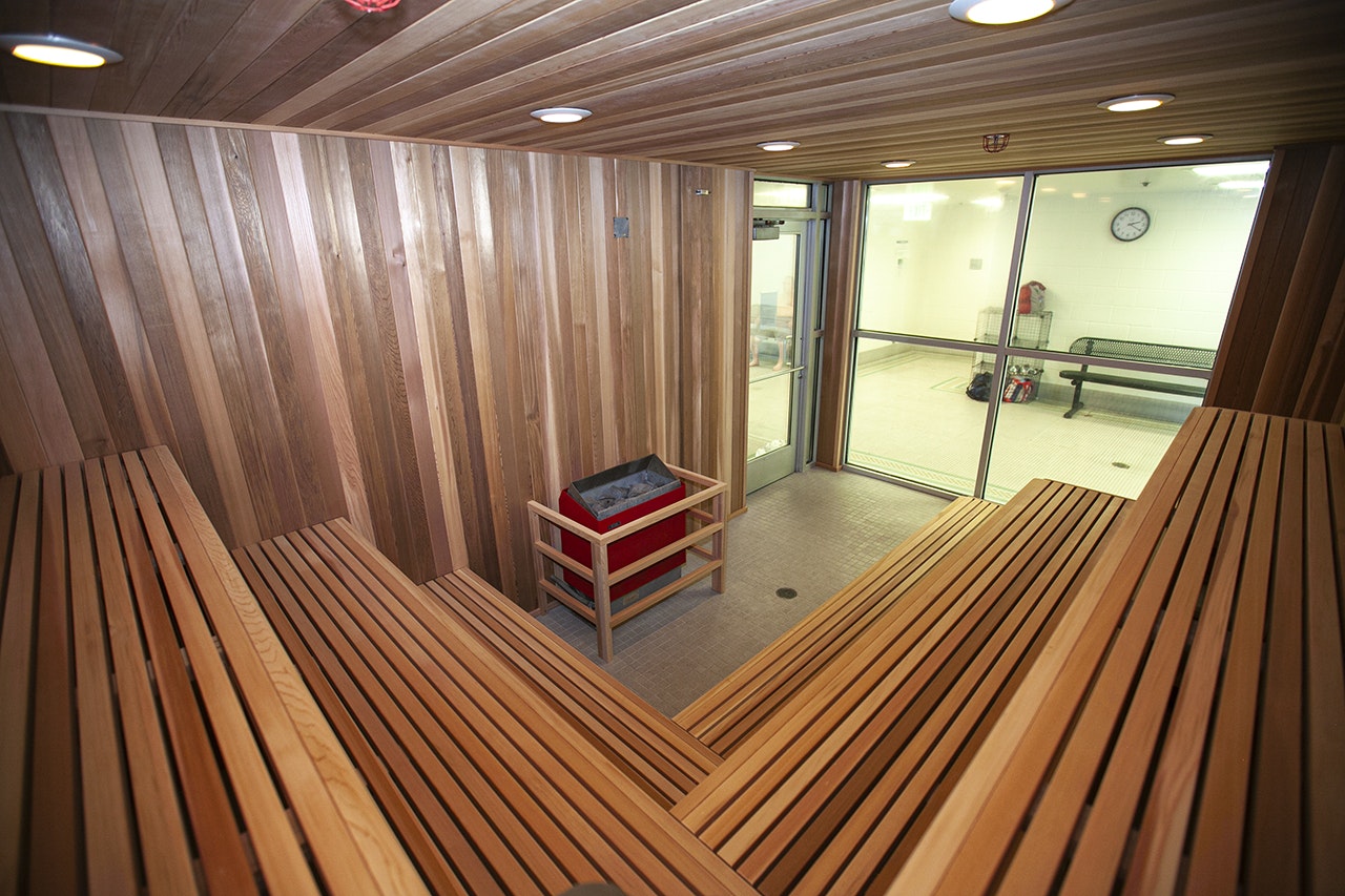 Interior of a sauna with wooden benches and a view of a relaxation area through a glass door.