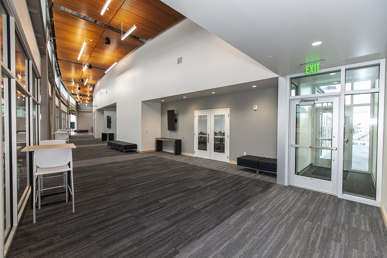 A modern interior hallway with seating areas, tables, wooden ceiling panels, and an exit door.