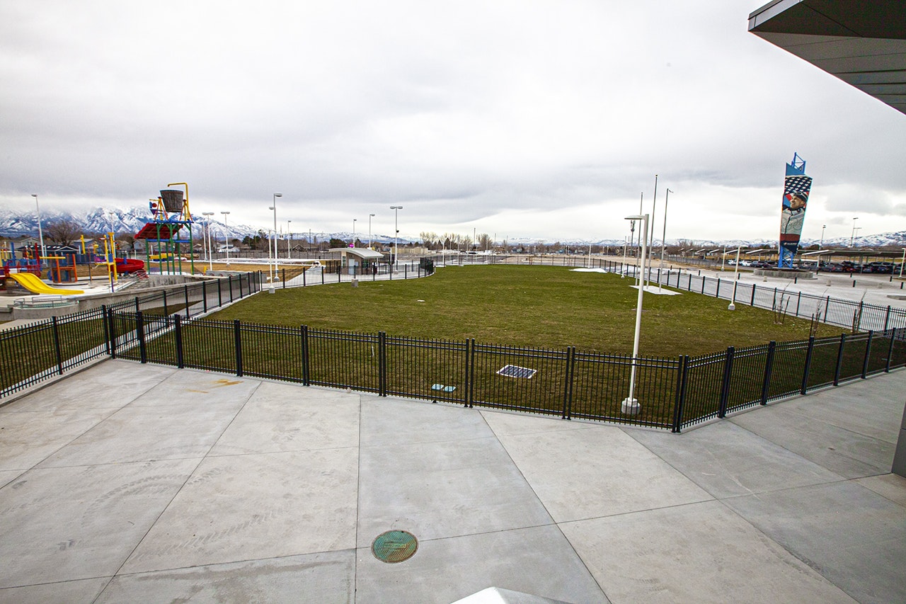 A fenced grassy area with playground and mountains in the distance, under a cloudy sky.