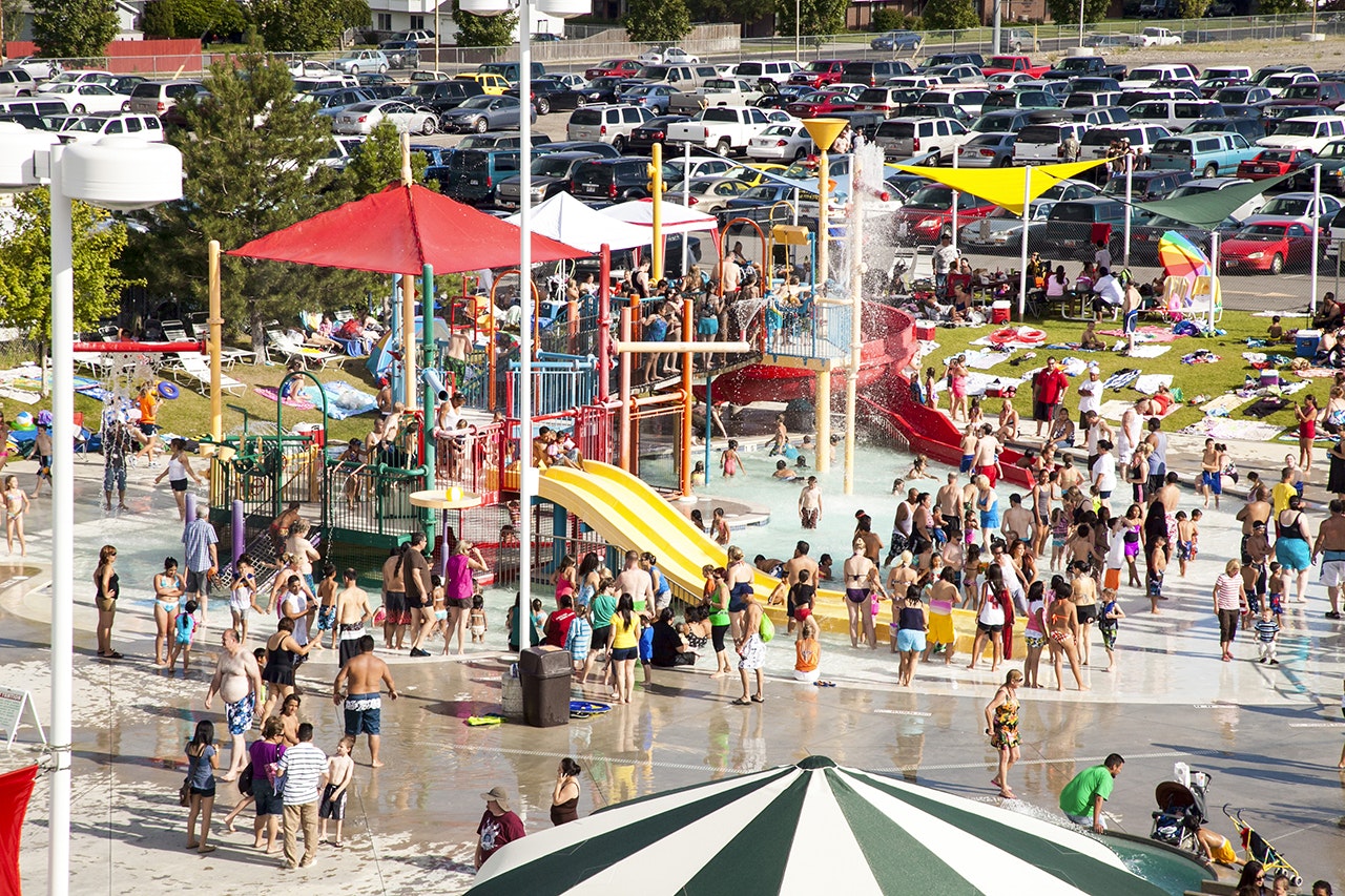 Crowded water park with slides, pools, umbrellas, and a packed parking lot.