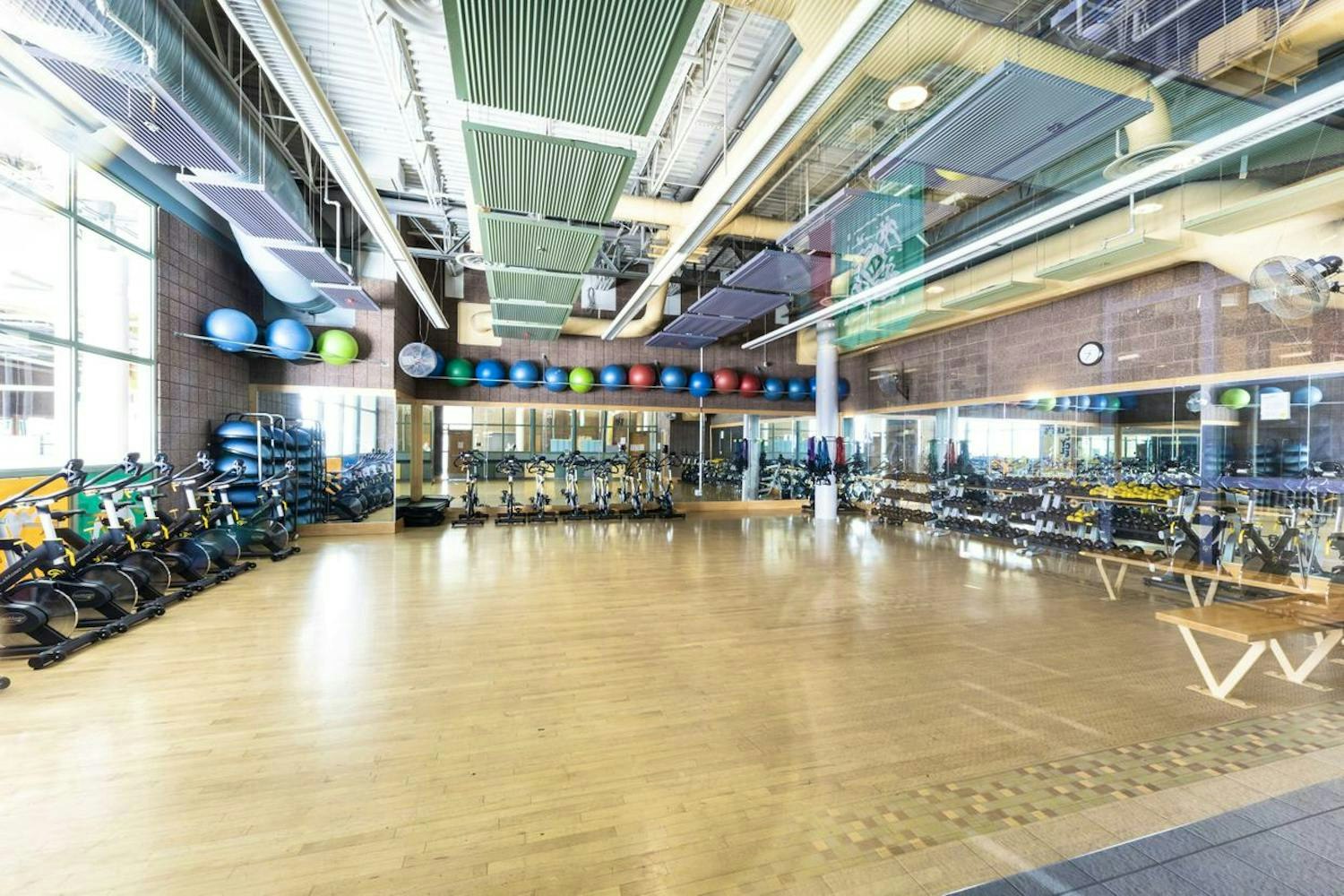 Modern gym interior with equipment, stationary bikes, colorful exercise balls, and wood flooring. No people visible.