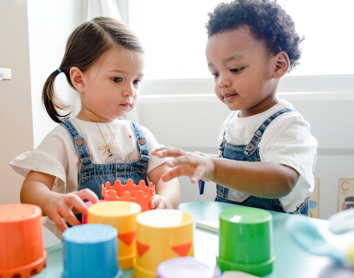 Two toddlers playing with colorful stacking cups on a table.