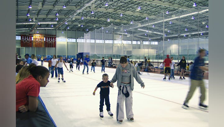 An indoor ice skating rink filled with people skating, a child and adult in the foreground.