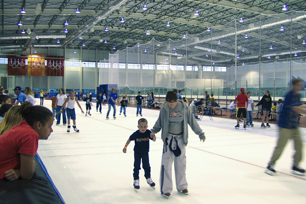 An indoor ice skating rink filled with people skating, a child and adult in the foreground.