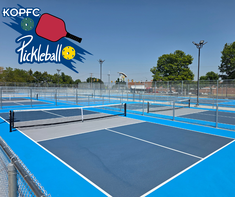 The image features a vibrant pickleball court with a logo and bright blue surfacing. Several fenced courts are visible under clear skies.