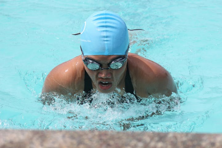 Swimmer in cap and goggles emerging from water.