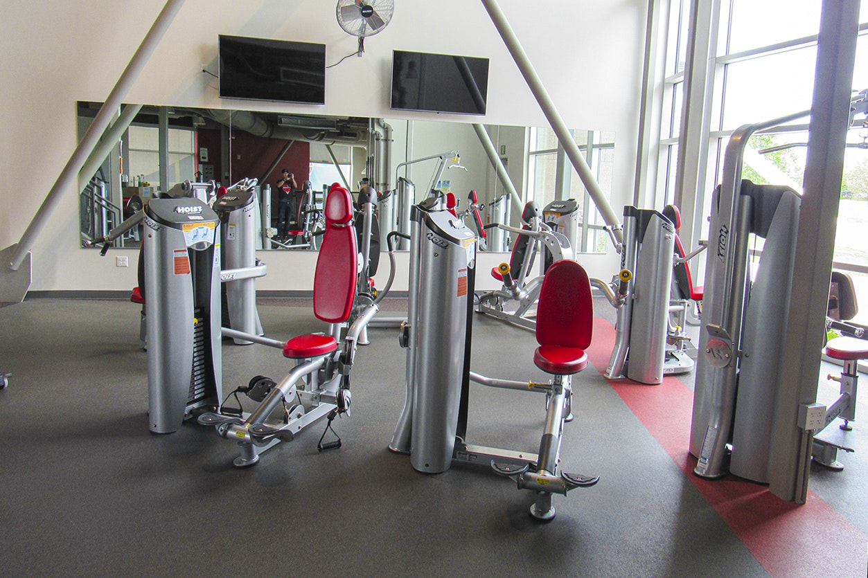 A gym with various exercise machines, TV screens, and large windows.