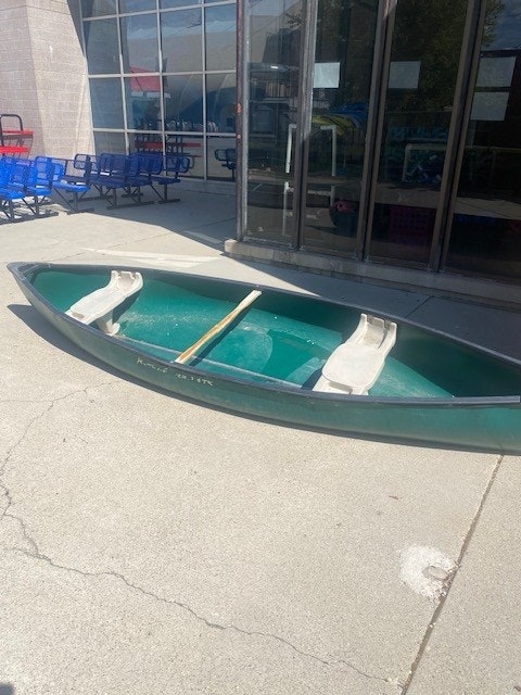 A green canoe with paddles outside a building.
