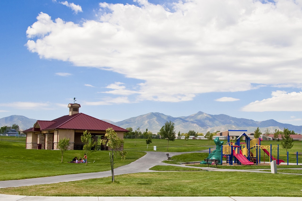 Pavilion, playground, mountains, blue sky, and clouds. People enjoying a sunny day at the park.