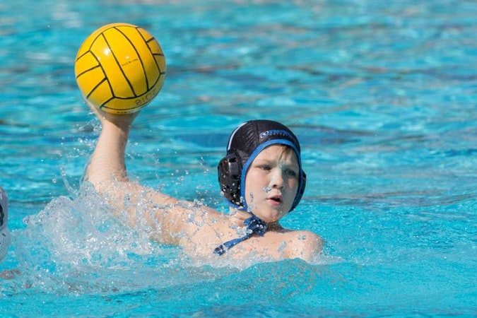 A water polo player in a cap is throwing a yellow ball in the pool.