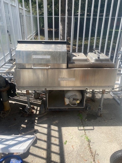 A stainless steel outdoor grill with closed lid, on a patio, next to a white fence.