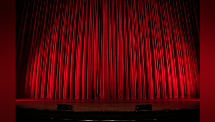 A red stage curtain closed with stage edge and two speakers visible.