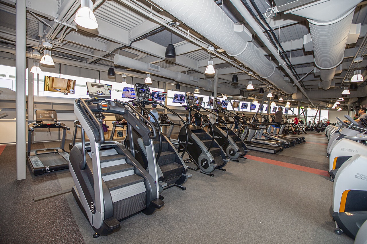 A well-equipped gym with treadmills and stair-stepper machines, TVs, and industrial-style lighting.