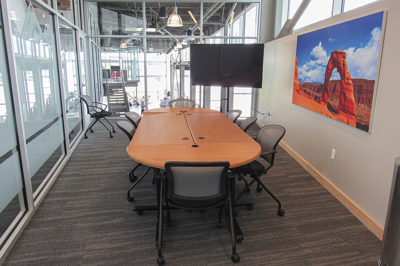 Modern conference room with a large table, chairs, a landscape painting on the wall, and a TV screen.