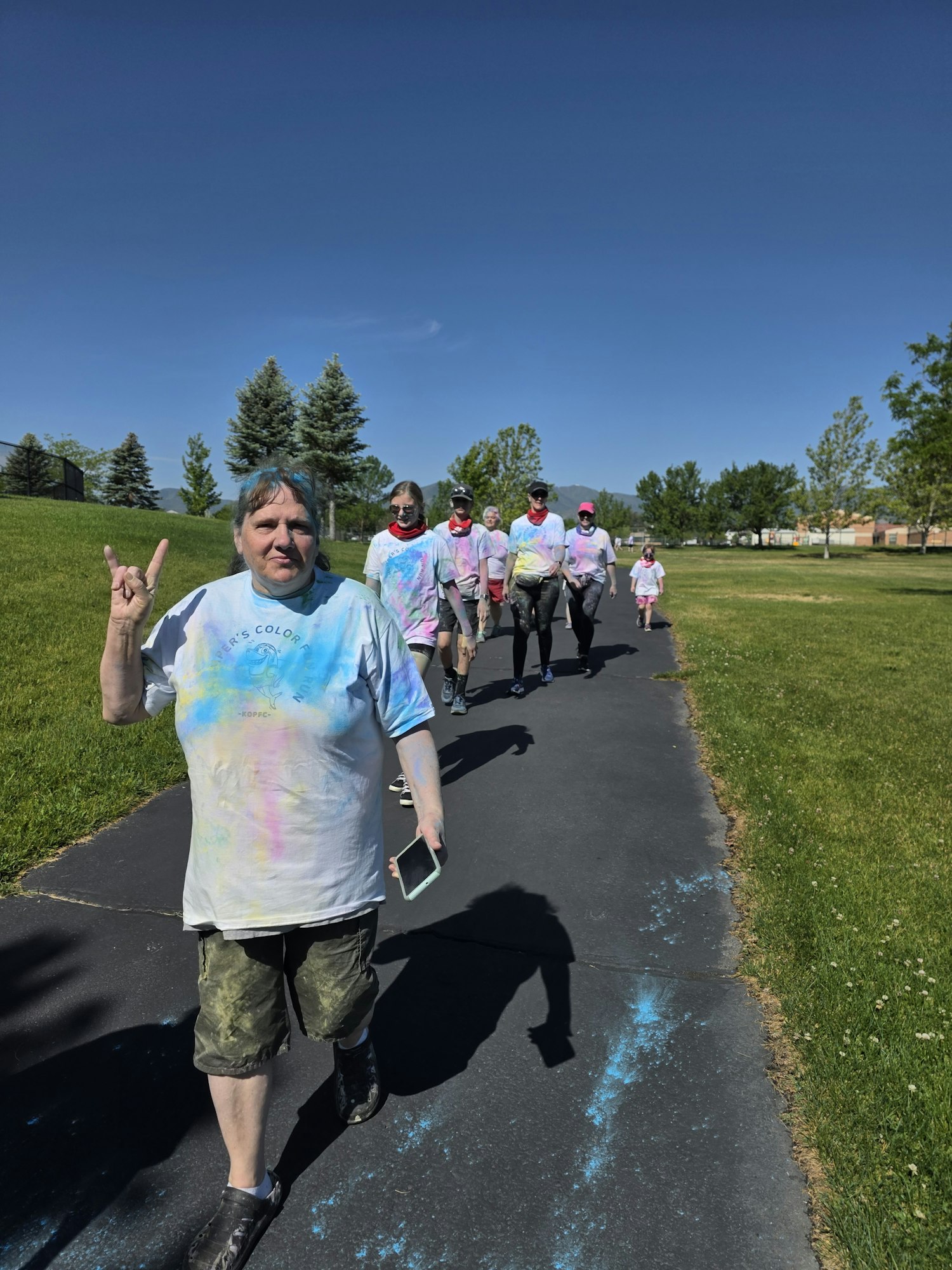 A group of people in colorful shirts is walking on a path in a grassy area under a clear blue sky.