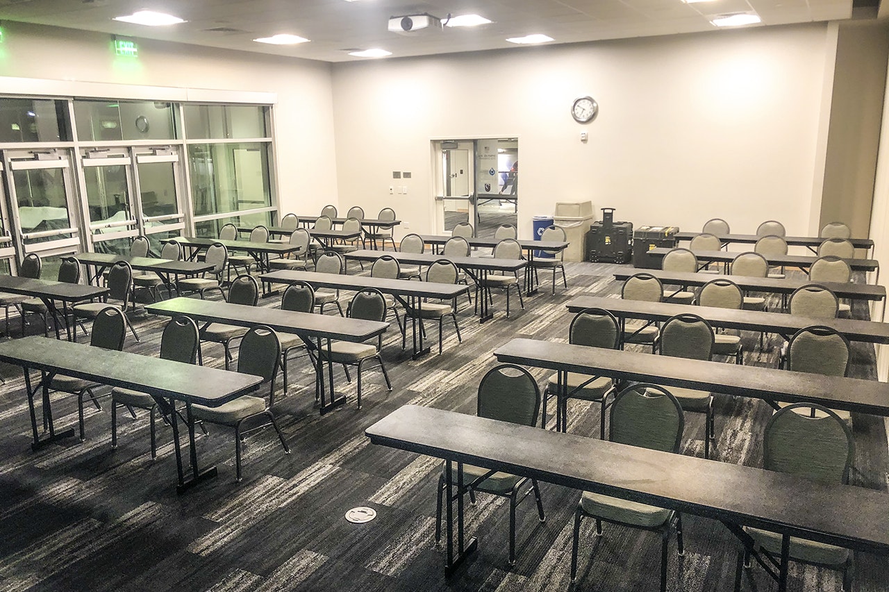 An empty classroom with tables, chairs, a clock on the wall, and a door at the back.