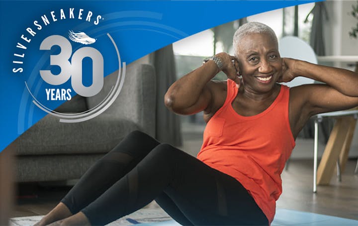 An elderly woman exercising at home, celebrating "SilverSneakers" 30th anniversary with a festive logo.