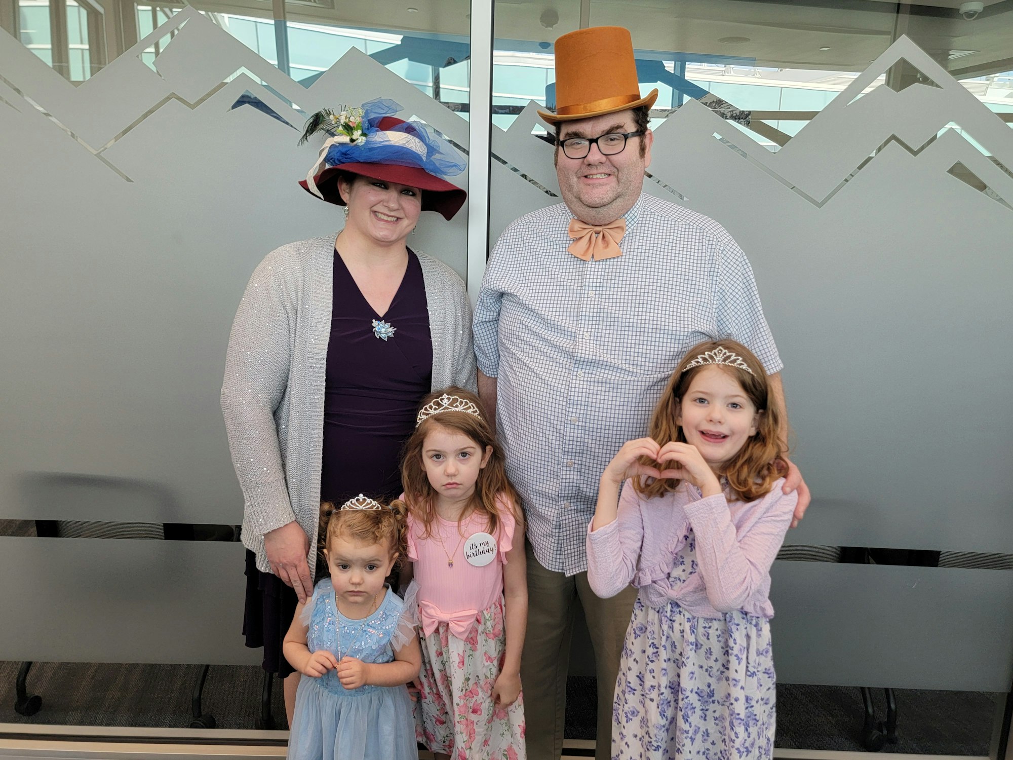 A family dressed in hats and tiaras posing in front of a decorated wall.