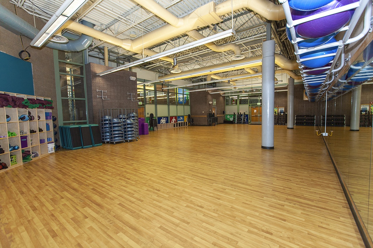 An empty fitness studio with exercise balls racked overhead, mirrors, and workout mats stored beside the room.