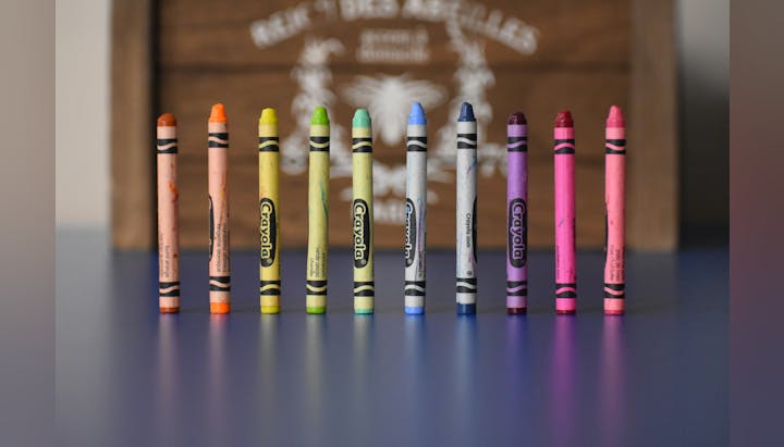 A row of colorful, used crayons with a cardboard box in the background.
