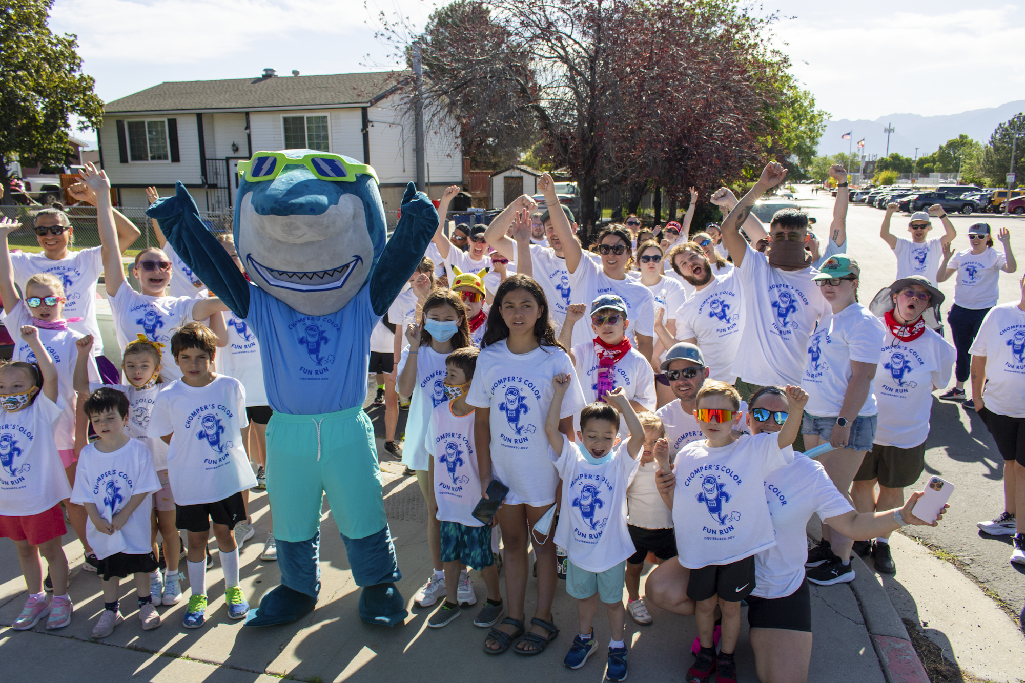 A group of people of all ages standing with a shark mascot while cheering.