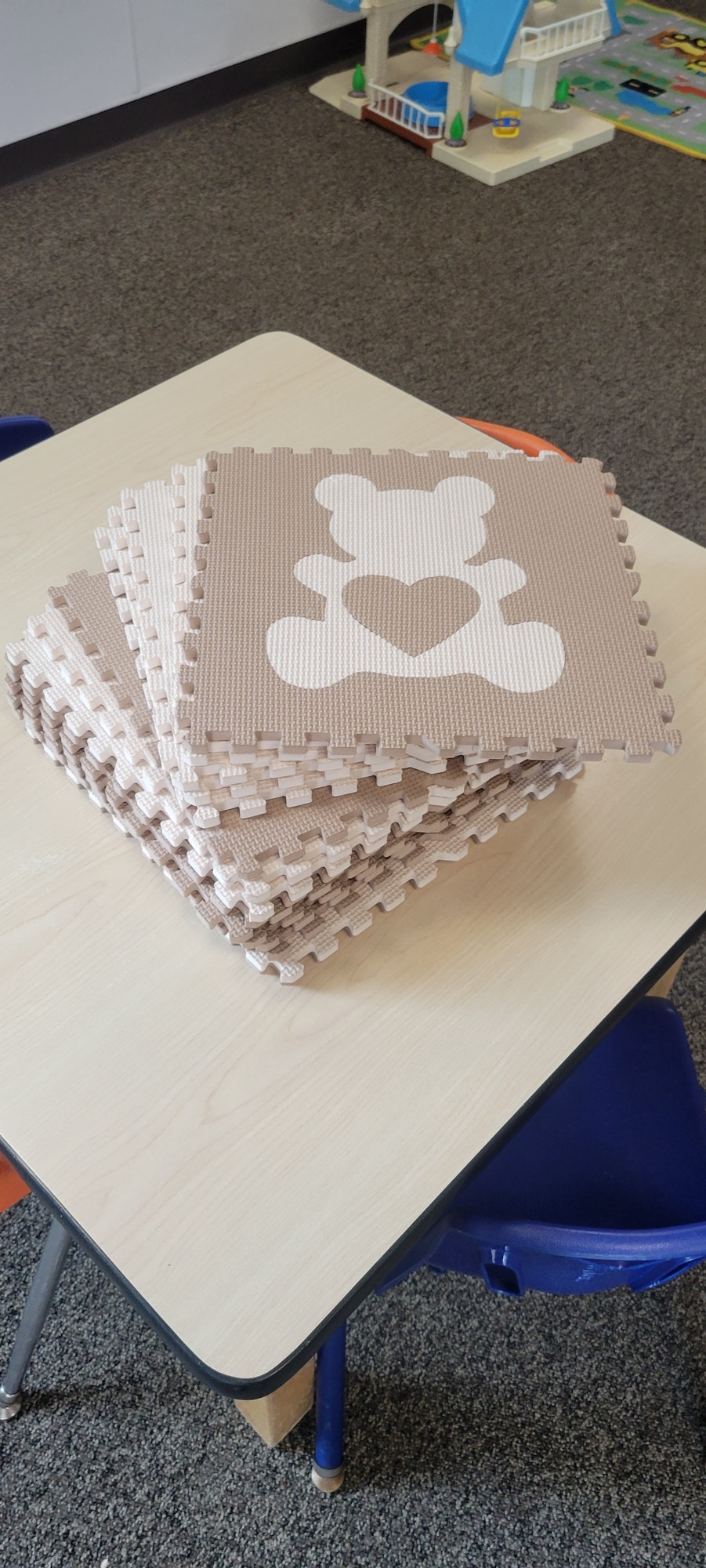 A puzzle mat on a table with pieces pulled out, forming an incomplete paw print design, a toddler's playhouse toy in the background.