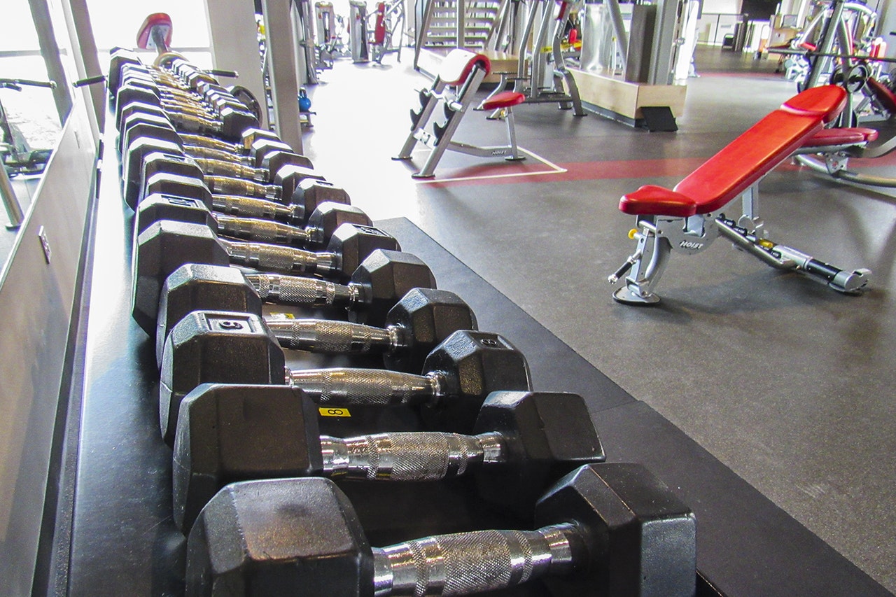 A row of dumbbells on a rack in a gym with exercise benches in the background.