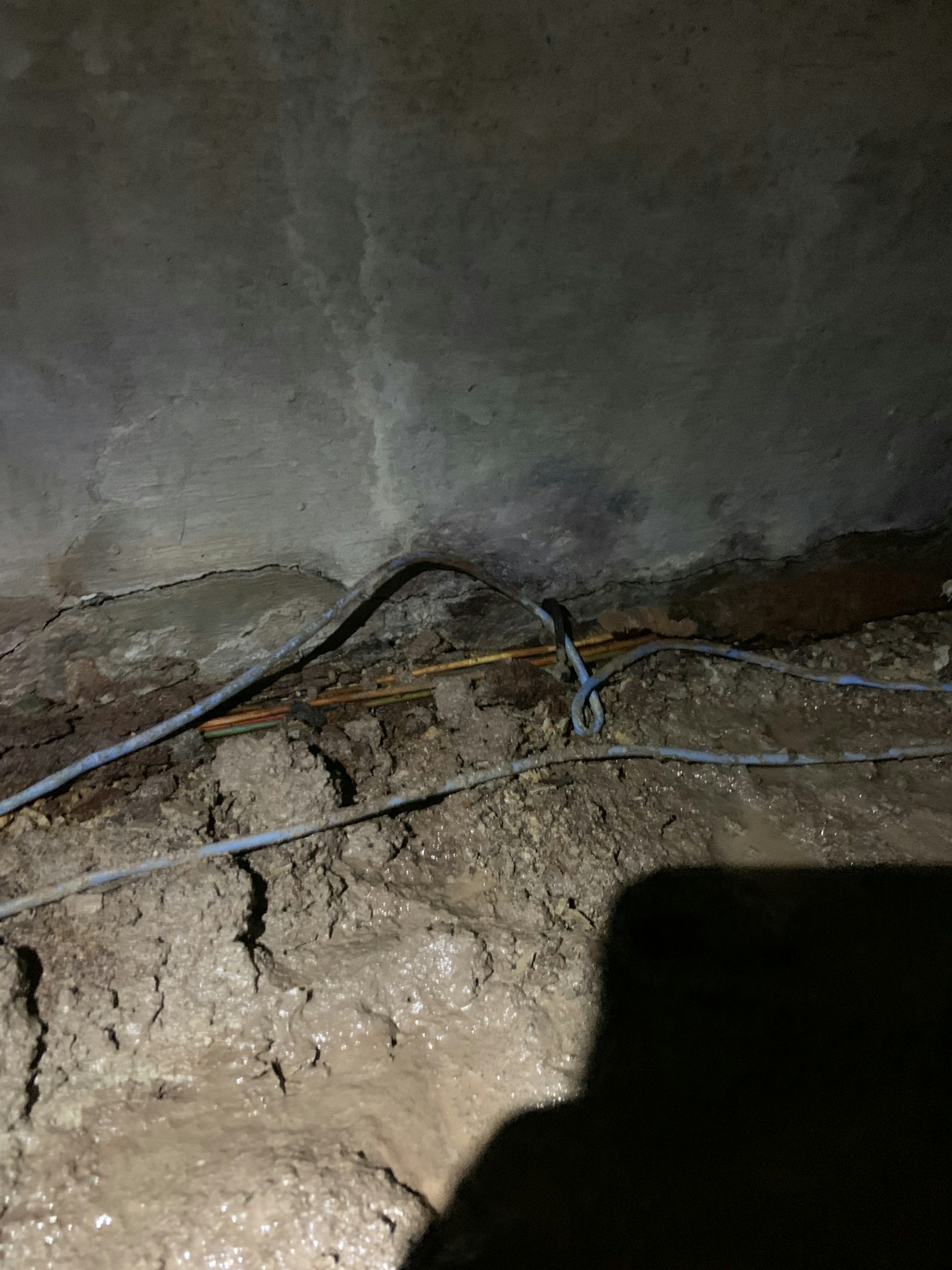A rough wall with exposed electrical wiring and cables tied together, possibly in a basement or underground area.
